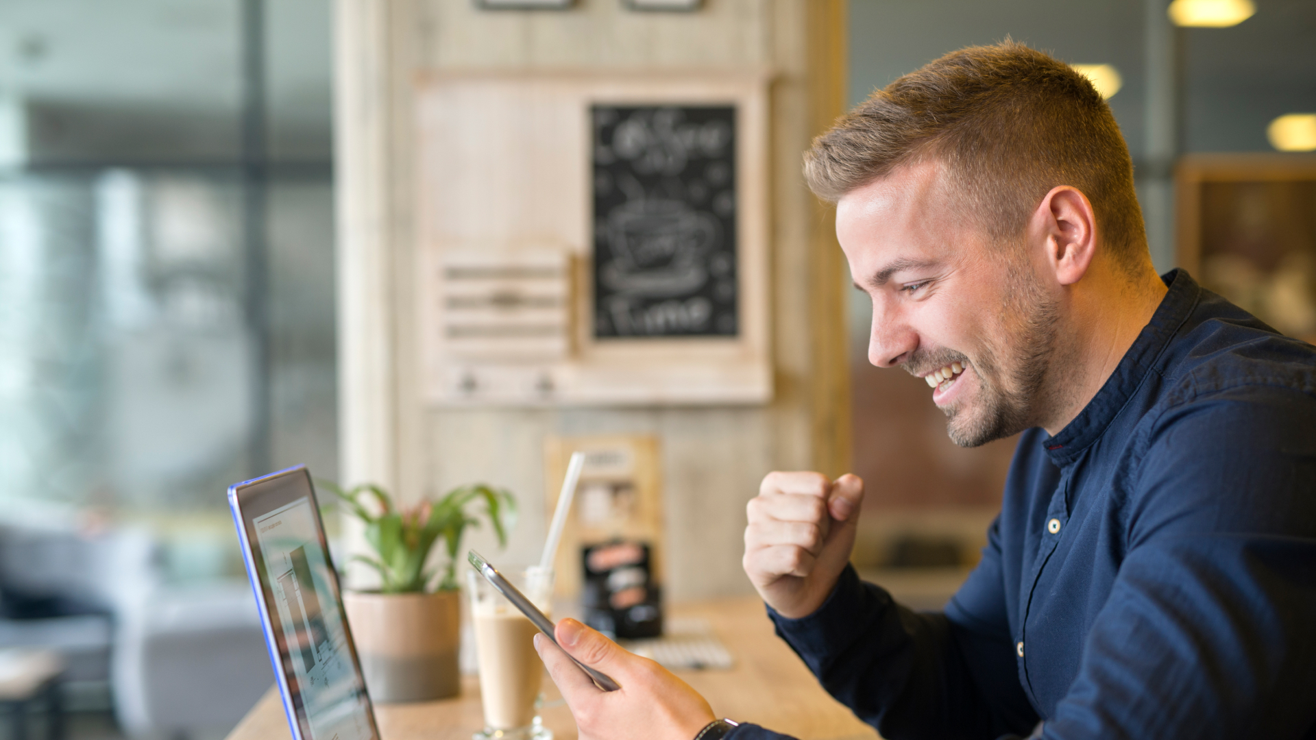 Empreendedor sorridente comemorando resultados positivos em notebook e smartphone após treinamento estratégico da Fenicio.