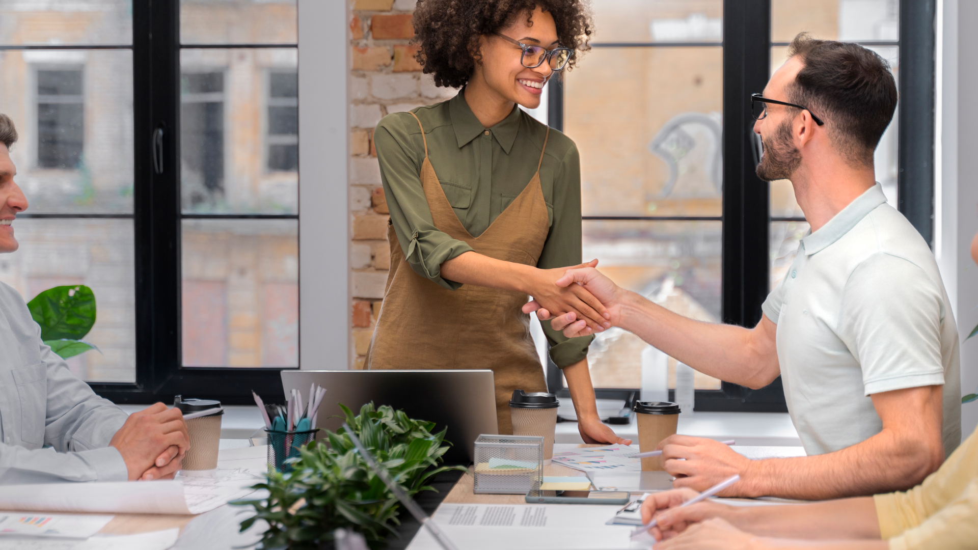 Consultora da Fenicio sorridente apertando a mão de aluno em mesa de treinamento corporativo, representando networking e troca de conhecimento.