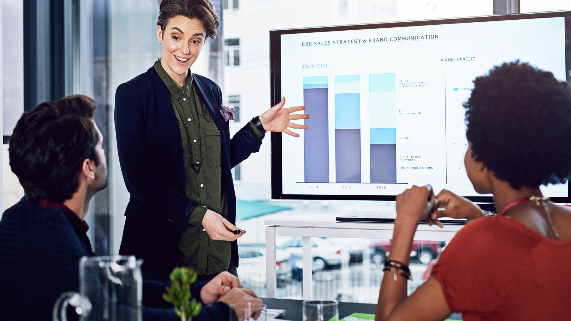 Consultora da Fenicio apresentando workshop de B2B Sales Strategy e Brand Communication com gráficos de performance em tela digital.